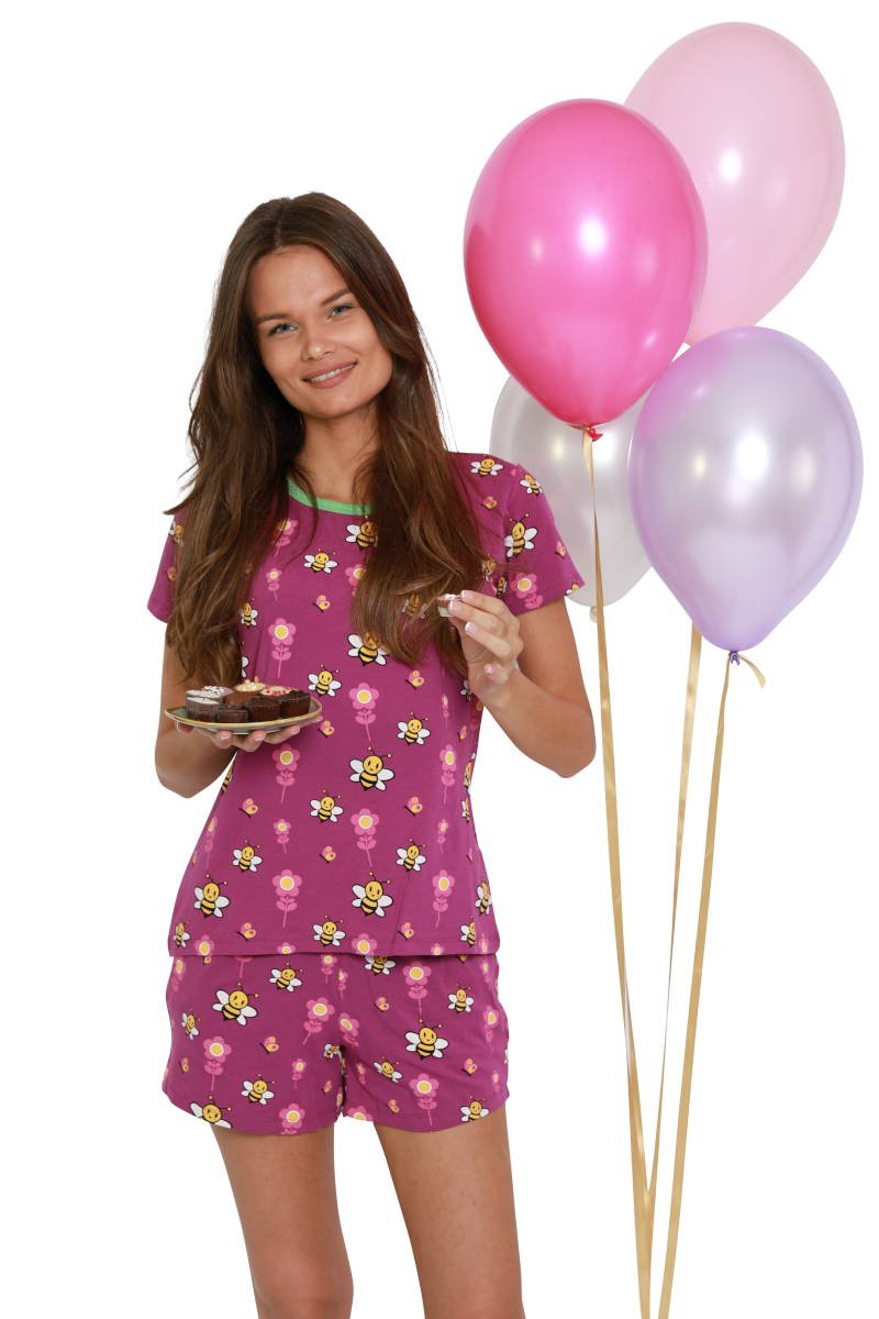 Vrouw eet bonbons in haar paarse dames shortama en viert een feestje met ballonnen