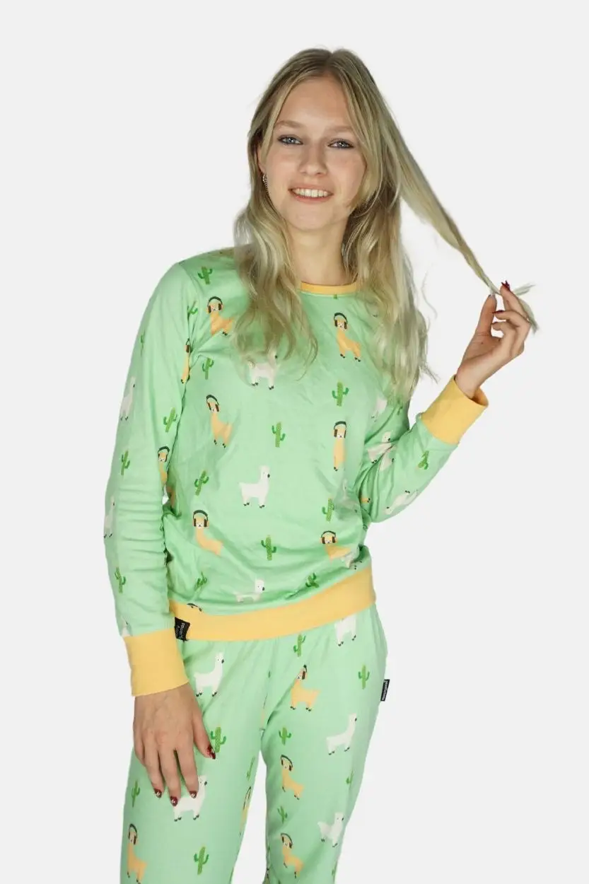 Model houd een pluk haar vast. Blond jong model lacht in de camera en een lichtgroene grappige alpaca pyjama. Bordes zijn lichtoranje en van elastiek met ribstof.